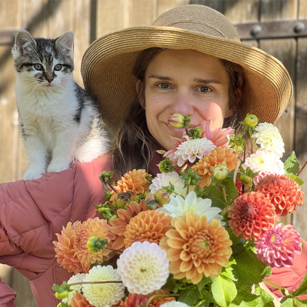 Camille Condomine and her cat with a handful of colorful dahlia blooms